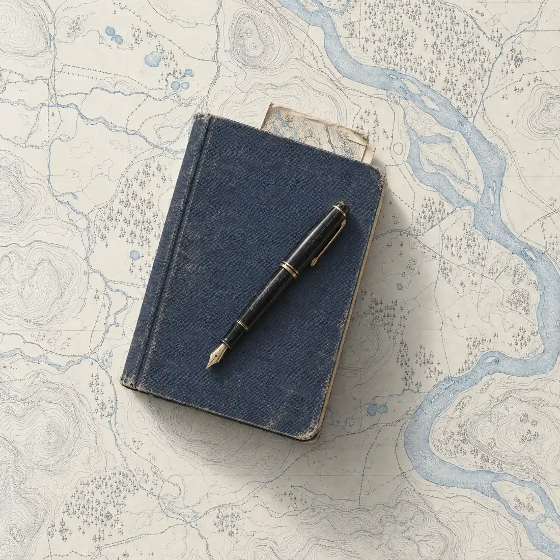 Blue cloth-bound notebook with a black fountain pen on top, on an engraved map